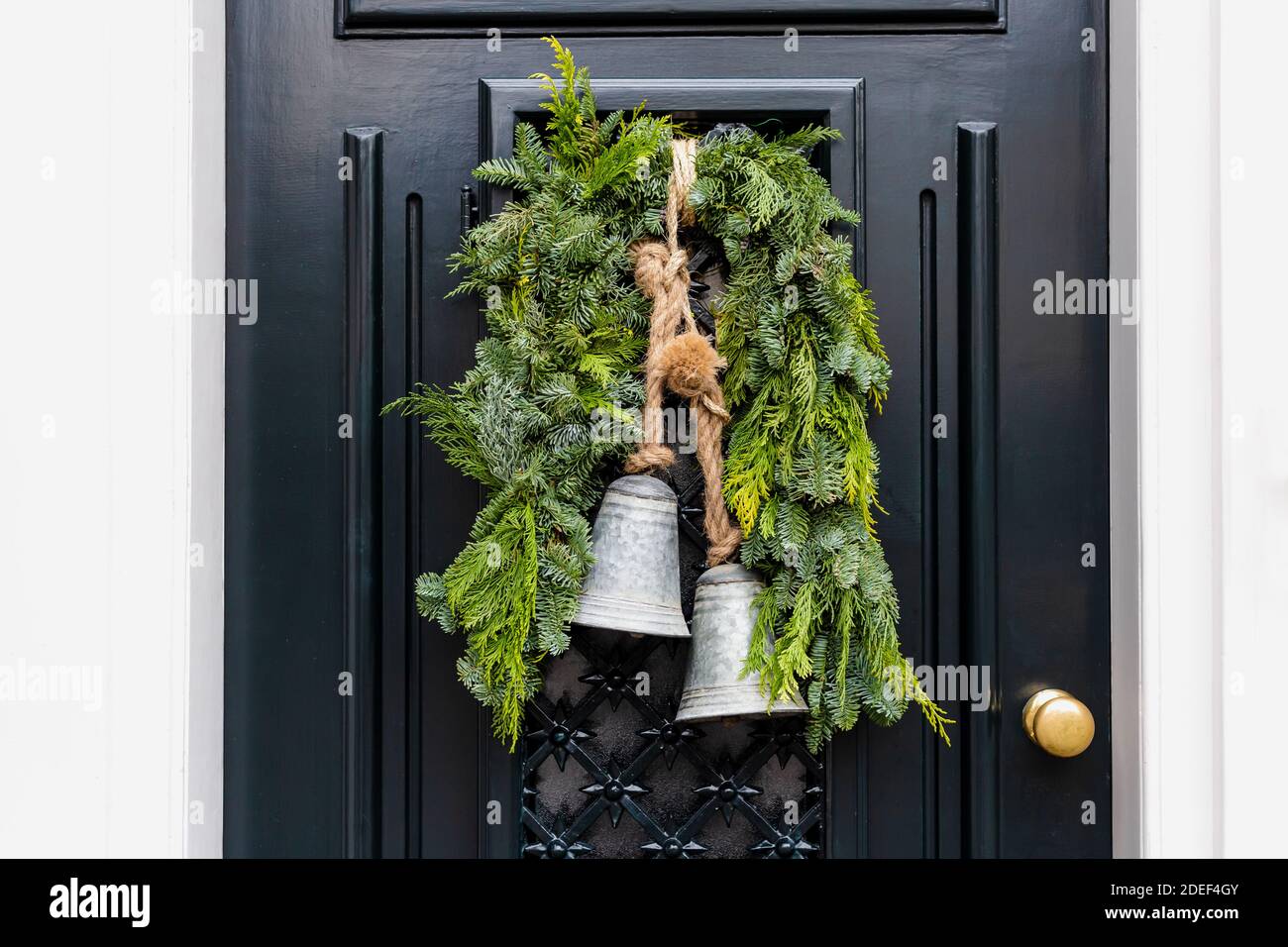 Corona di Natale con campane all'ingresso porta nera annata all'esterno. Veranda porta anteriore decorata con decorazioni natalizie wreath. Tradizionale Foto Stock