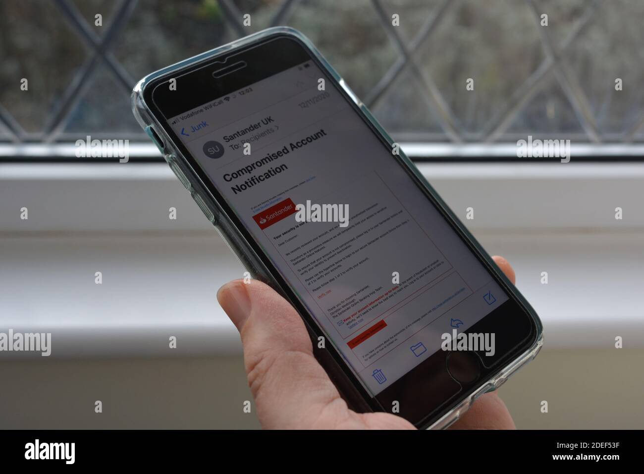 Telefono cellulare in mano alla donna con un messaggio e-mail di phishing/truffa, che si suppone provenga dalla banca Santander, visualizzato sullo schermo Foto Stock