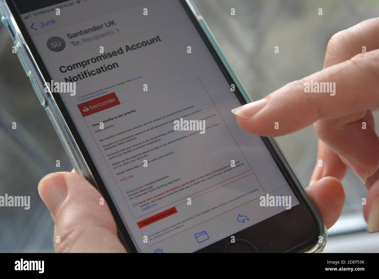 Telefono cellulare in mano alla donna con un messaggio e-mail di phishing/truffa, che si suppone provenga dalla banca Santander, visualizzato sullo schermo Foto Stock