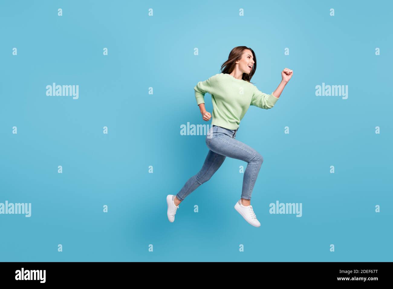 Lunghezza intera corpo dimensione laterale profilo foto di abbastanza giovane ragazza che corre in avanti veloce saltando sorridente isolato su vibrante sfondo di colore blu Foto Stock