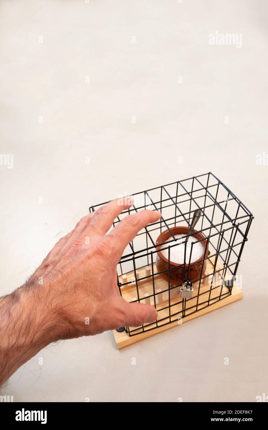 mano cercando di tenere un barattolo di zucchero all'interno di una gabbia bloccata, concetto di ansia, tentazione, perdita di peso, dieta senza zucchero verticale Foto Stock