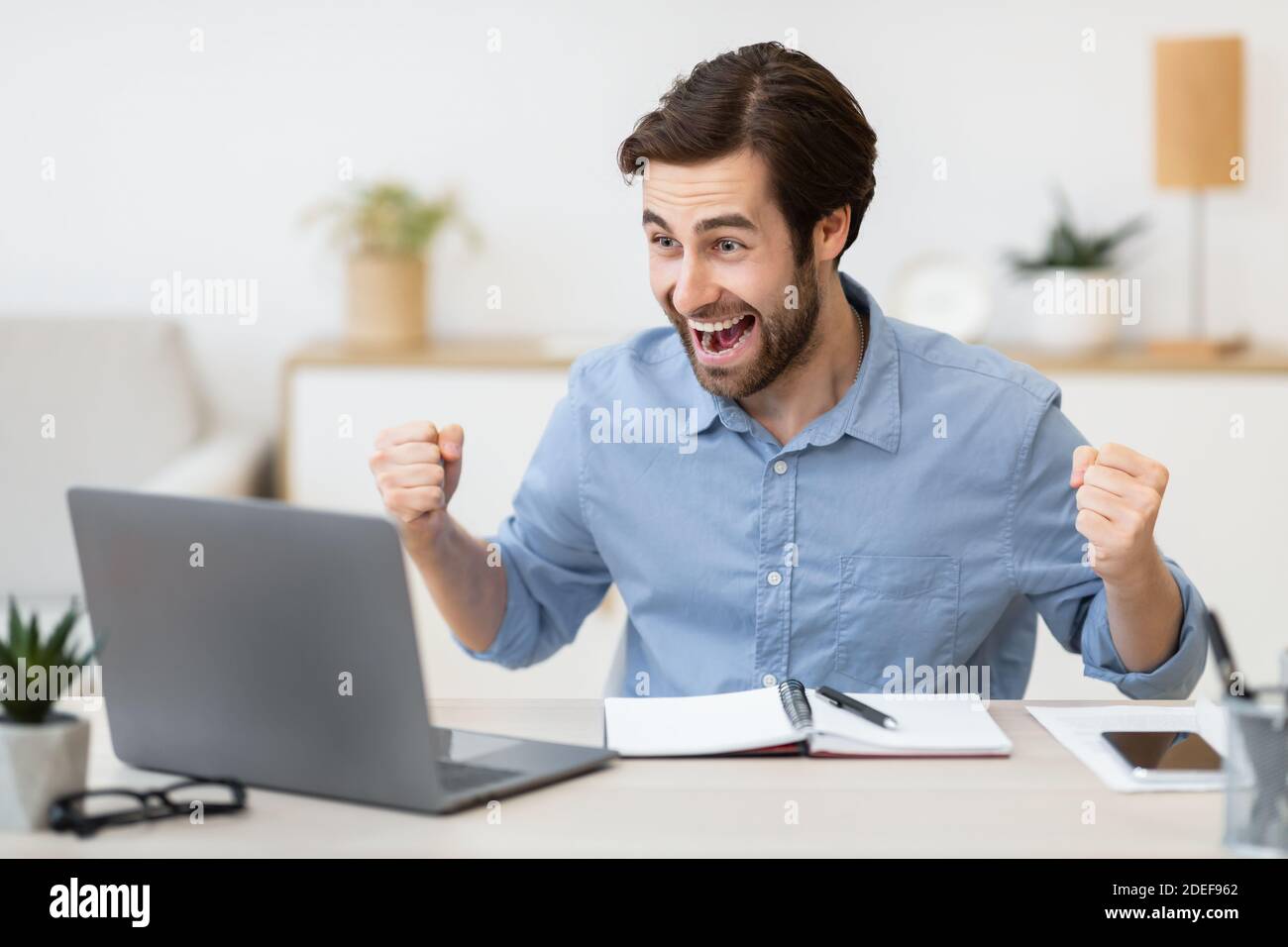Eccitato giovane uomo d'affari al computer portatile scuotendo i Fists in ufficio Foto Stock