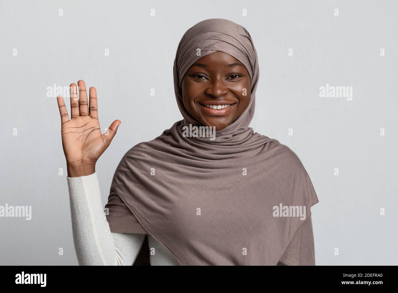 Ciao Gesture. Amichevole Black Muslim Lady in sciarpa mano sventolante a Camera Foto Stock