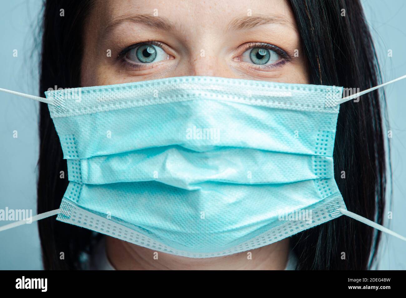 Donna con gli occhi blu mette una maschera medica Foto Stock