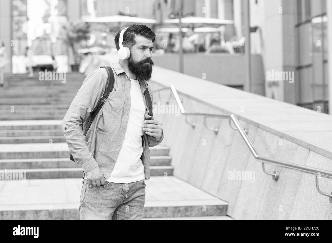 Percorso giornaliero al lavoro. Vita moderna. Modifica del concetto di scenario. Bello hipster con zaino strada a piedi. Camminando per strade vuote. Uomo con cuffie che cammina nel centro della città. Ascoltare musica. Foto Stock