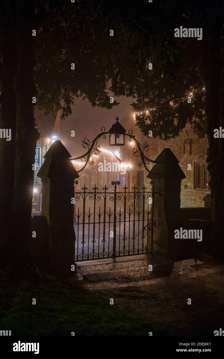 Le porte della chiesa di St Edwards e le luci di natale lungo la strada della chiesa nella nebbia di notte. Stow sul Wold, Cotswolds, Gloucestershire, Inghilterra Foto Stock