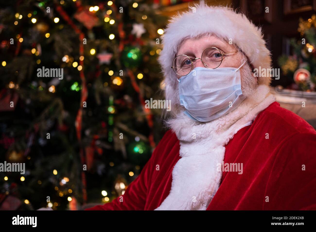 Babbo Natale in maschera medica. Ritratto positivo Santa seduta vicino albero di Natale. Felice anno nuovo Covid 2021 Foto Stock