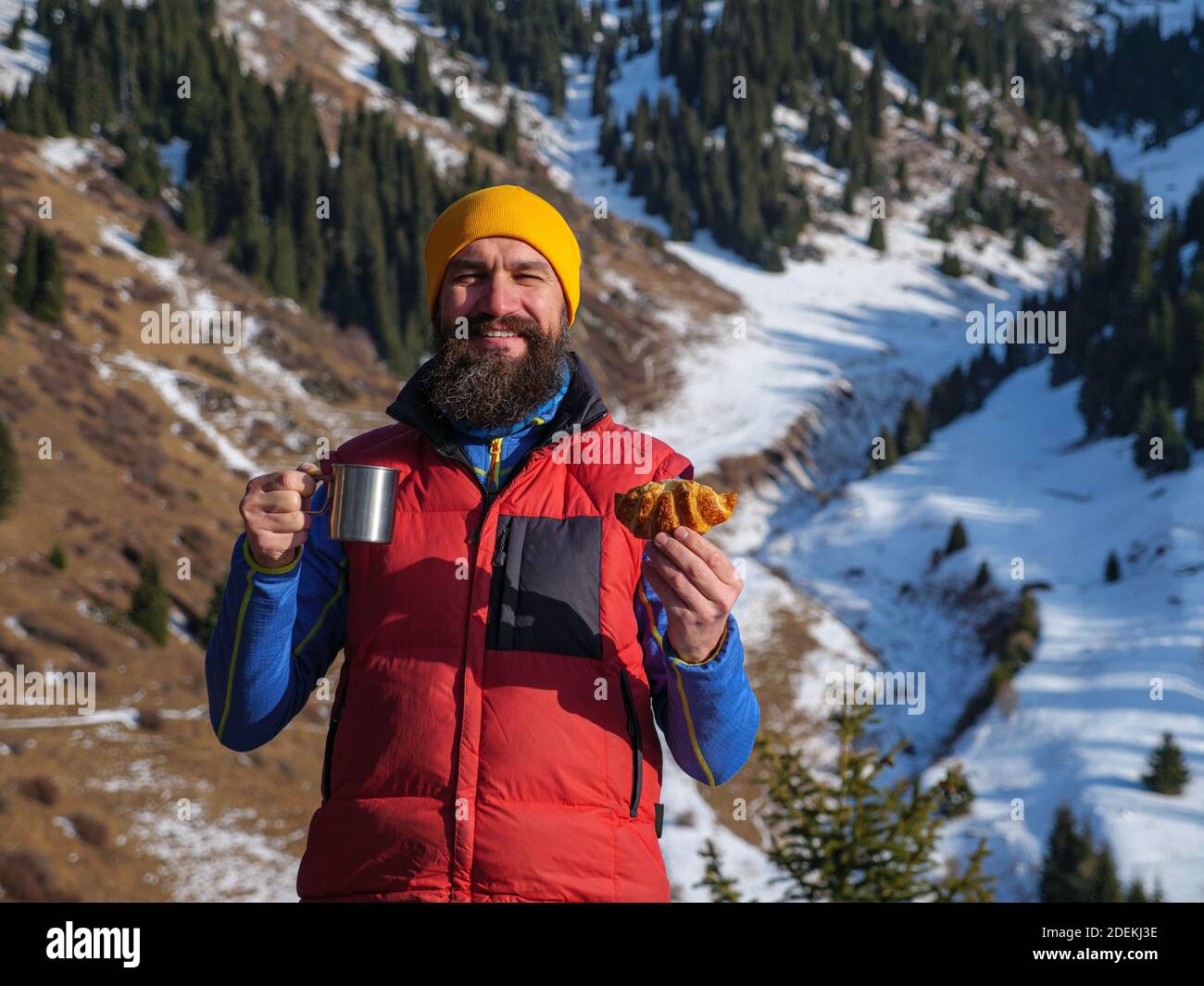 Ritratto di un viaggiatore maschile con un bicchiere di bevanda in mano. L'uomo fa escursioni all'aperto in inverno in montagna Foto Stock