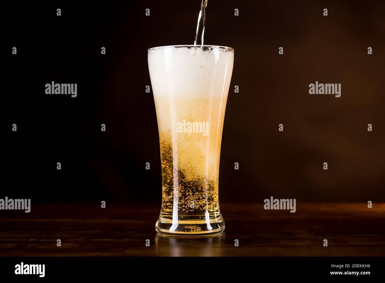 Birra fredda dorata versata nel bicchiere con schiuma schiuma sulla parte superiore del tavolo di legno Foto Stock