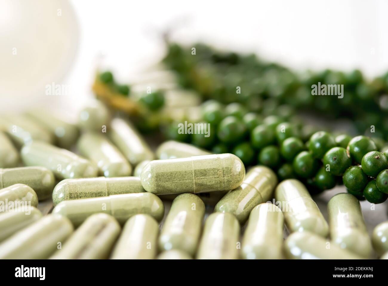 Primo piano della medicina biologica naturale asiatica di erbe in forma di capsule con pepe verde sullo sfondo Foto Stock
