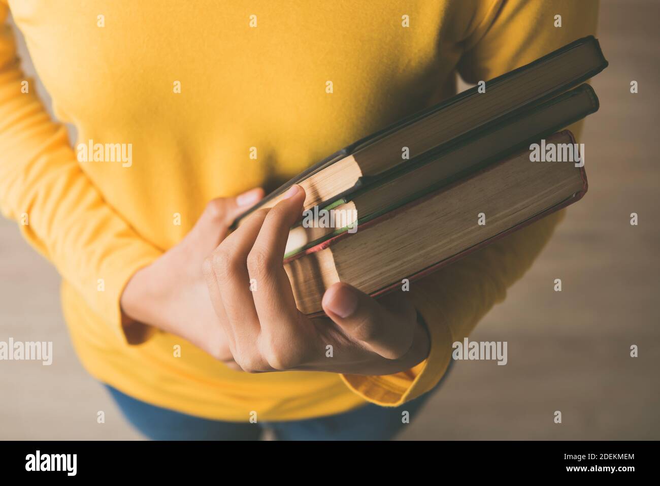 Mani di studentessa in maglione giallo che porta i libri dentro una biblioteca per studiare la sua ricerca di assegnazione di classe - formazione concetto Foto Stock