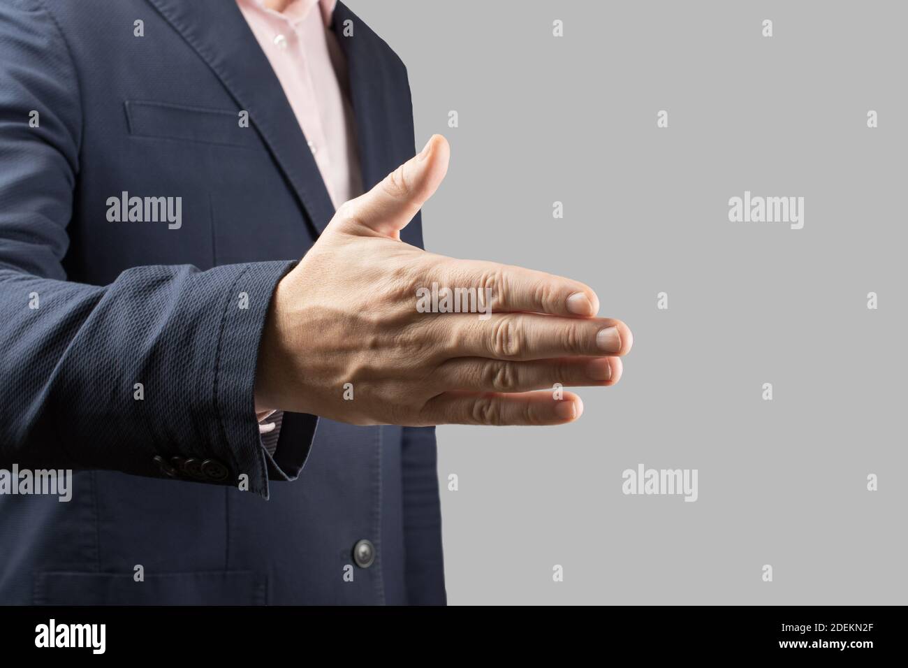 uomo d'affari maschile tiene la mano per una stretta di mano su uno sfondo grigio. Uomo d'affari e gesto argomento un uomo in un vestito e la cravatta tiene fuori la sua mano a. Foto Stock