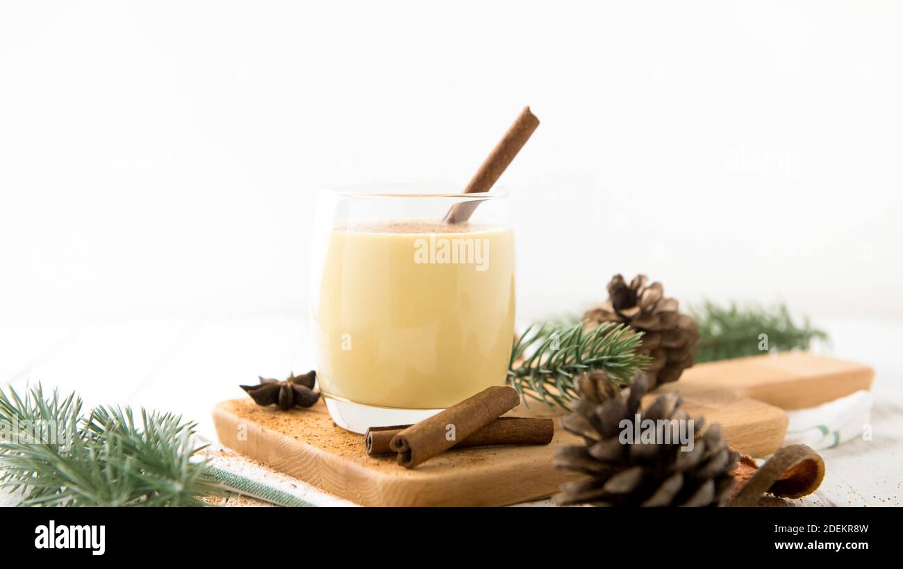 Bevanda casalinga tradizionale di Natale in un bicchiere con noce moscata macinata, cannella e oggetti decorativi su tavola di legno bianco, preparandosi per celebratina Foto Stock