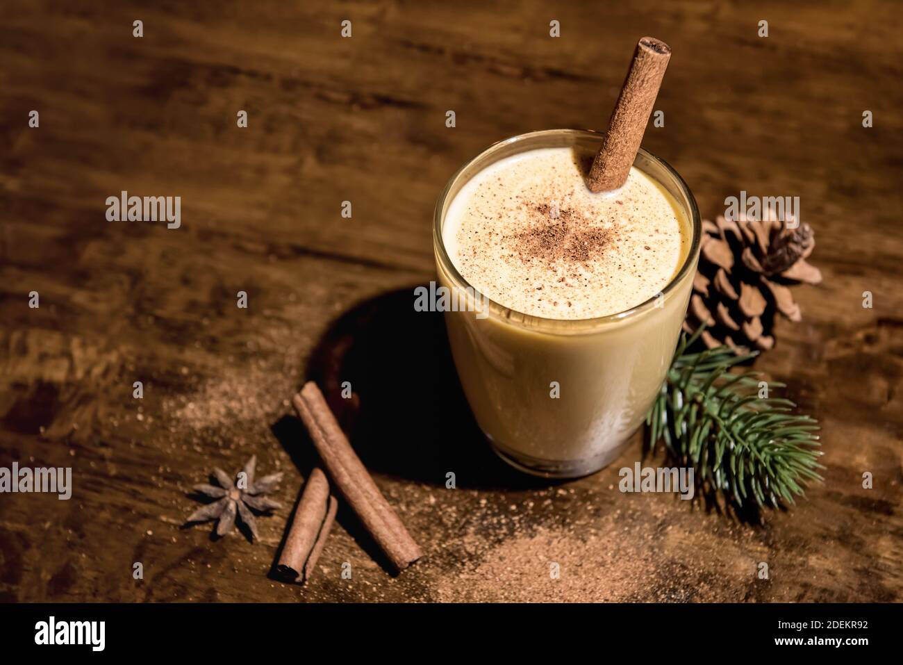 Bevanda casalinga tradizionale di Natale eggnog in un bicchiere con noce moscata macinata, cannella e oggetti decorativi su tavola di legno, preparandosi per celebrare il fest Foto Stock
