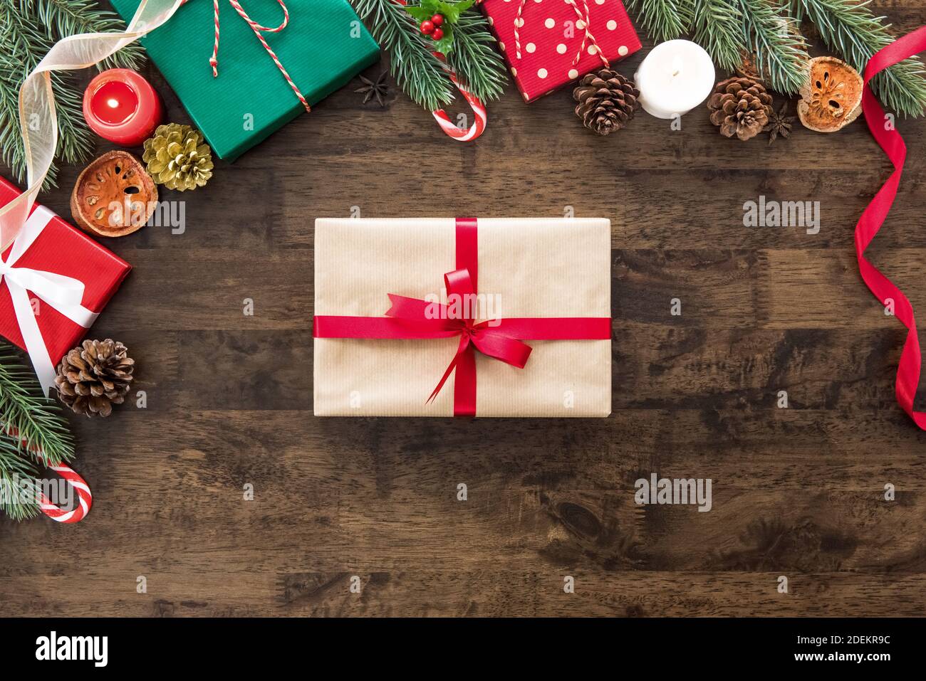 Regalo di Natale su tavola di legno con coloratissimi oggetti decorativi e scatole al confine, preparato per una persona speciale durante le festività natalizie Foto Stock