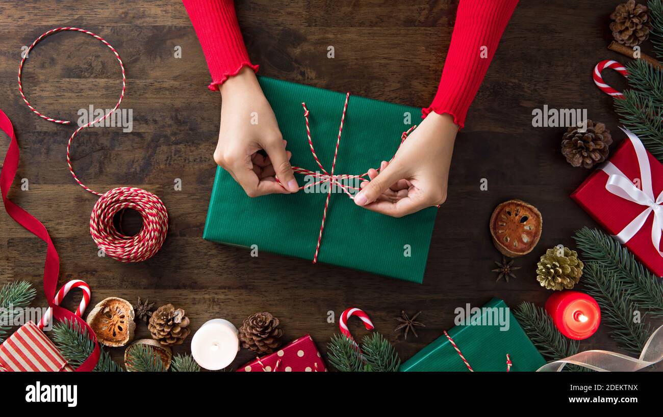 Donna in una scatola regalo di legatura del pullover rosso nel centro di natale decorazione oggetti su una tavola di legno preparazione per festeggiare la stagione festiva Foto Stock