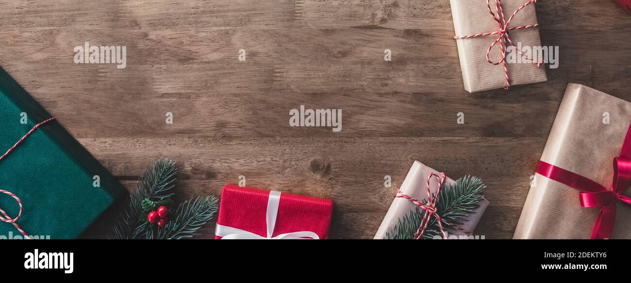 Scatole regalo natalizie decorate con pino e mistetoe su sfondo tavola in legno, bordo design vista dall'alto con spazio per testi - panne panoramica Foto Stock