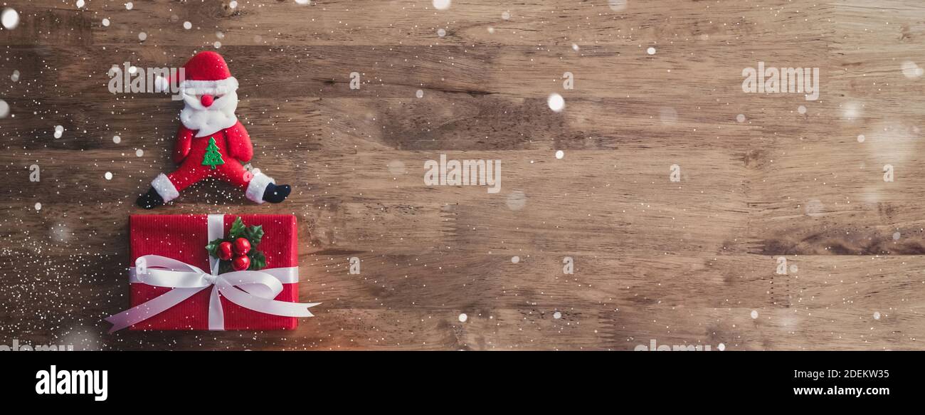 Bella festa di Natale top view banner sfondo, idea di design creativo, con scatole regalo rosso, Babbo Natale bambola e caduta neve effetto su tavola di legno Foto Stock