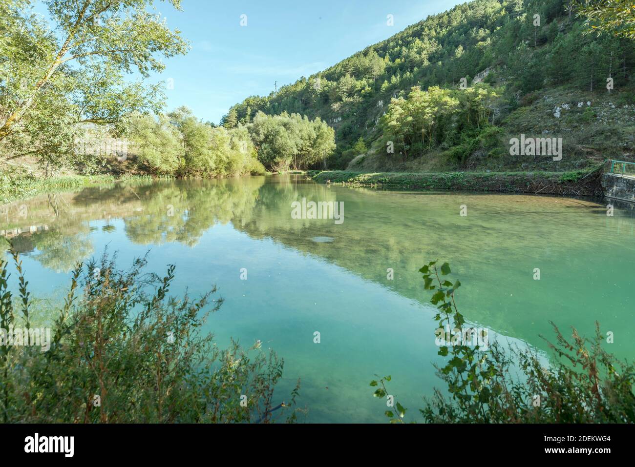 Paesaggio con acque limpide di laghetto formato dal fiume Giovenco tra pendii boscosi, sparato in luce intensa vicino a Pescina, l'Aquila, Abruzzo, Italia Foto Stock