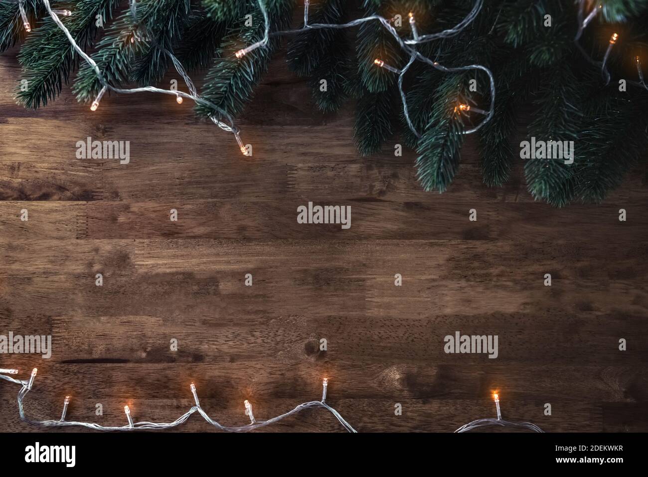 Lampeggiamento stringa di luce decorativa di Natale con foglie di pino verde su sfondo tavola di legno, vista dall'alto bordo disegno con spazio di copia Foto Stock