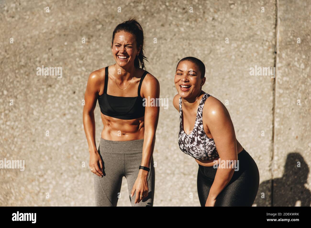 Due donne del fitness in piedi all'aperto la mattina. le donne in allenamento indossano un sorriso insieme contro un muro. Foto Stock