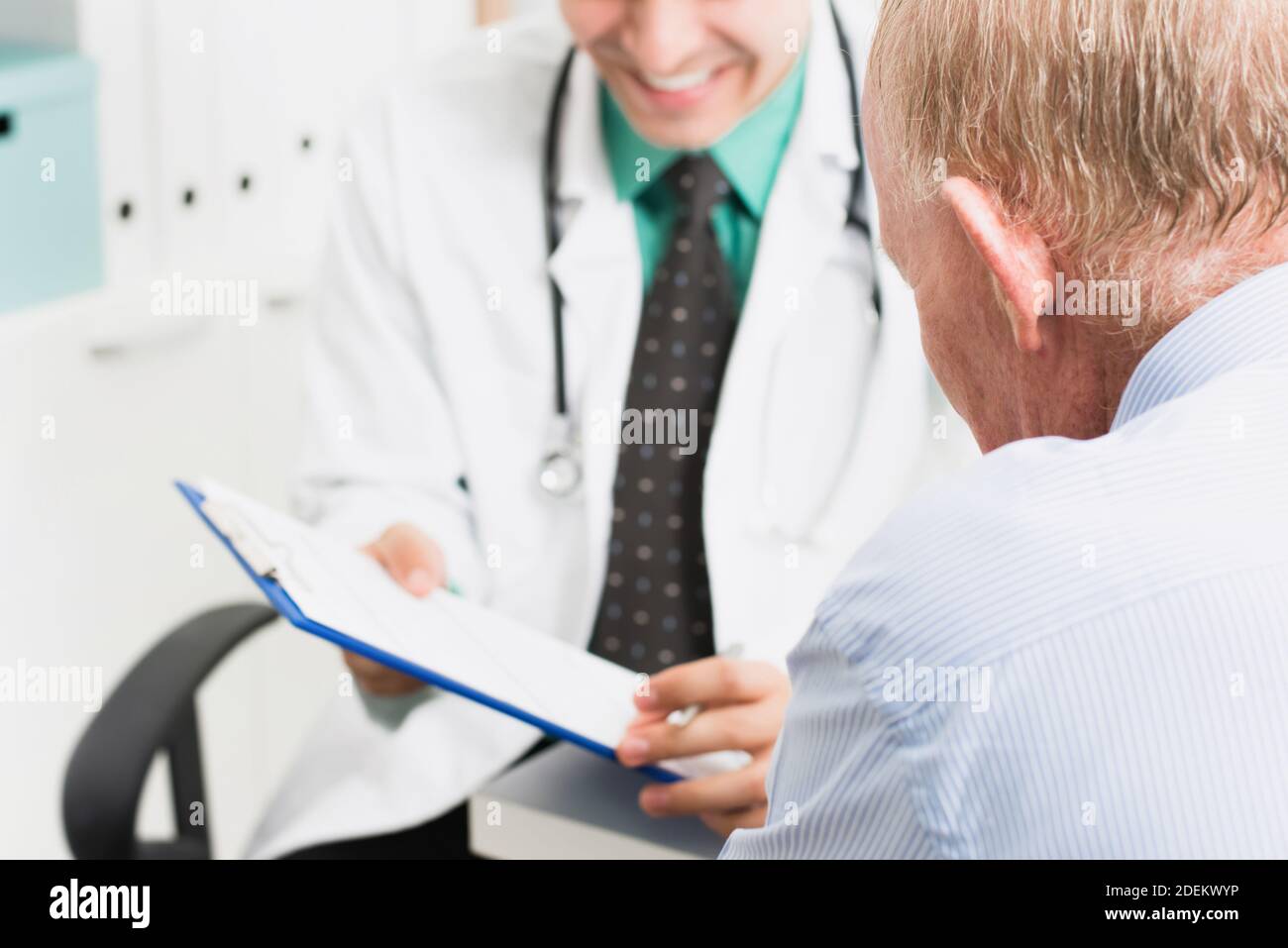 Paziente maschile senior che guarda la cartella clinica mentre si consulta con gentile medico sorridente in ospedale Foto Stock