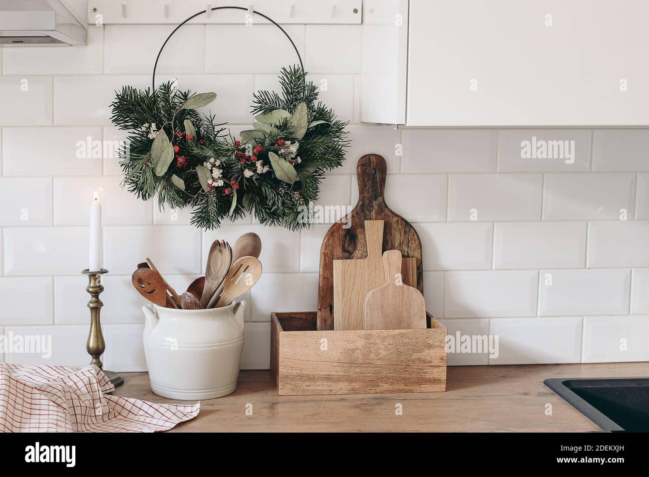 Primo piano dell'interno della cucina. Decorazione di Natale. La corona floreale dell'Avvento pende su rotaie a spina. Muro di mattoni bianchi, piastrelle della metropolitana, ripiani in legno Foto Stock