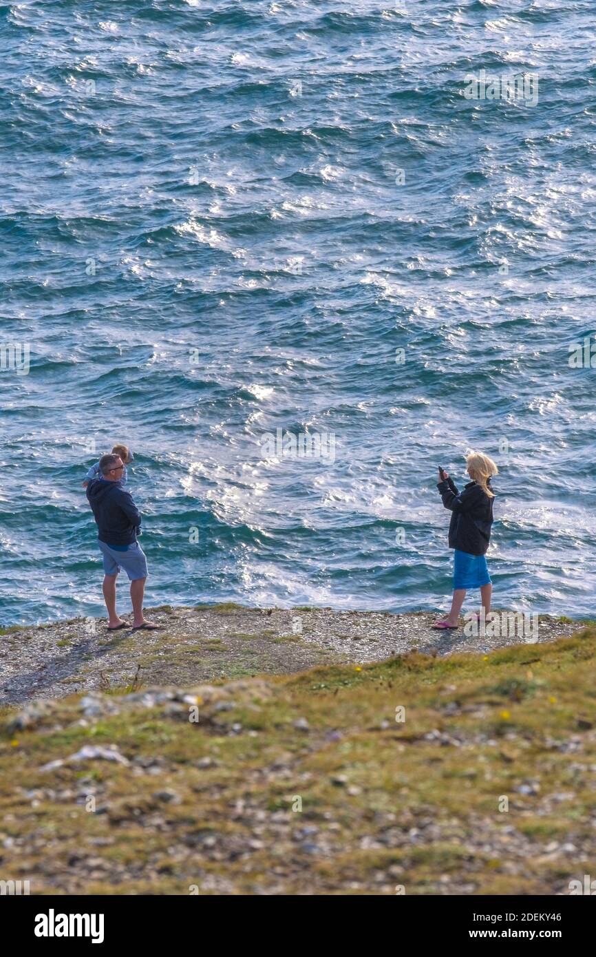 Una donna che usa il suo cellulare per scattare una fotografia di un uomo che tiene un bambino su un sentiero sulla costa a Newquay in Cornovaglia. Foto Stock