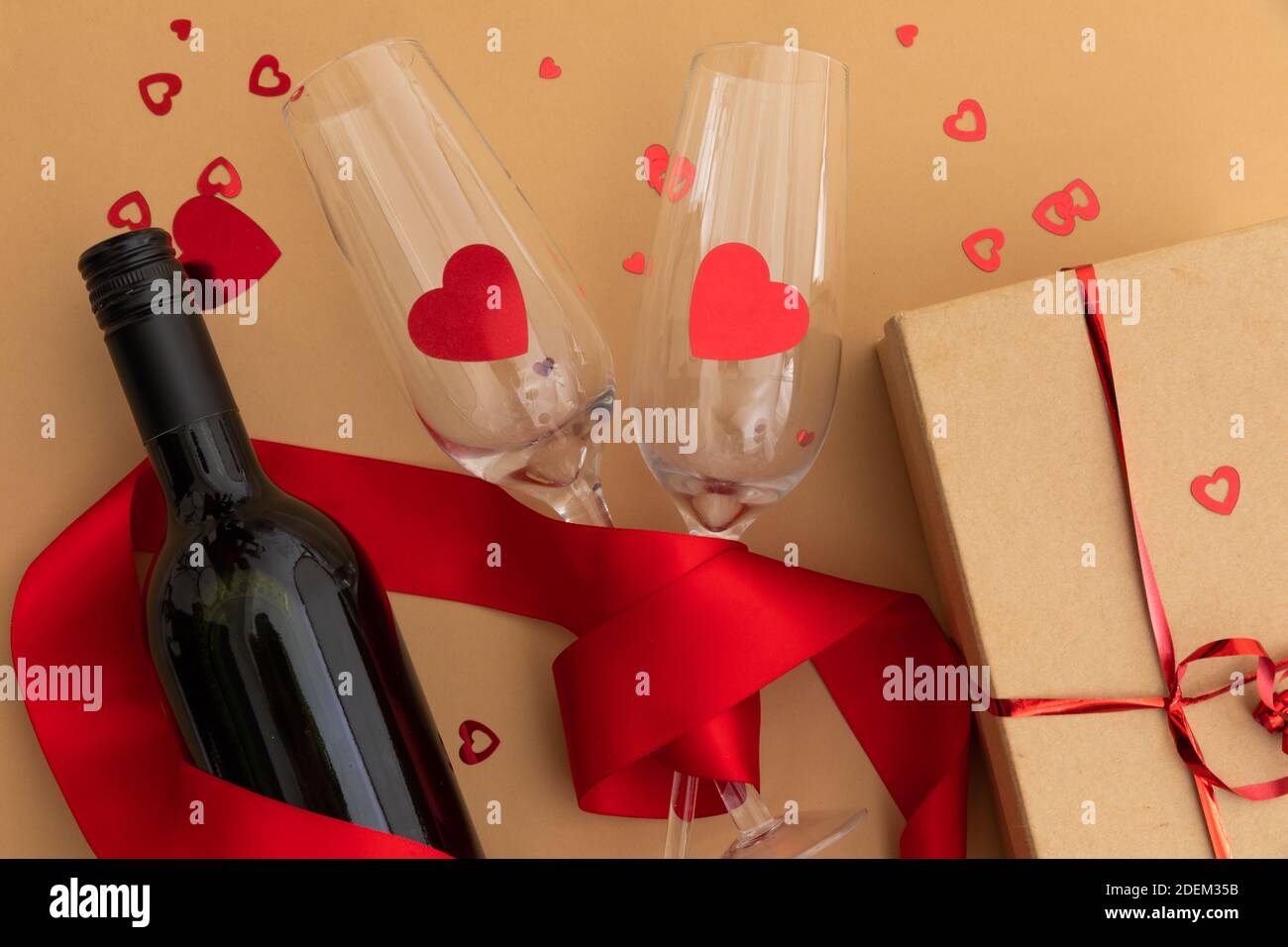 Bottiglia di vino, bicchieri con cuori rossi e presenti su fondo marrone Foto Stock