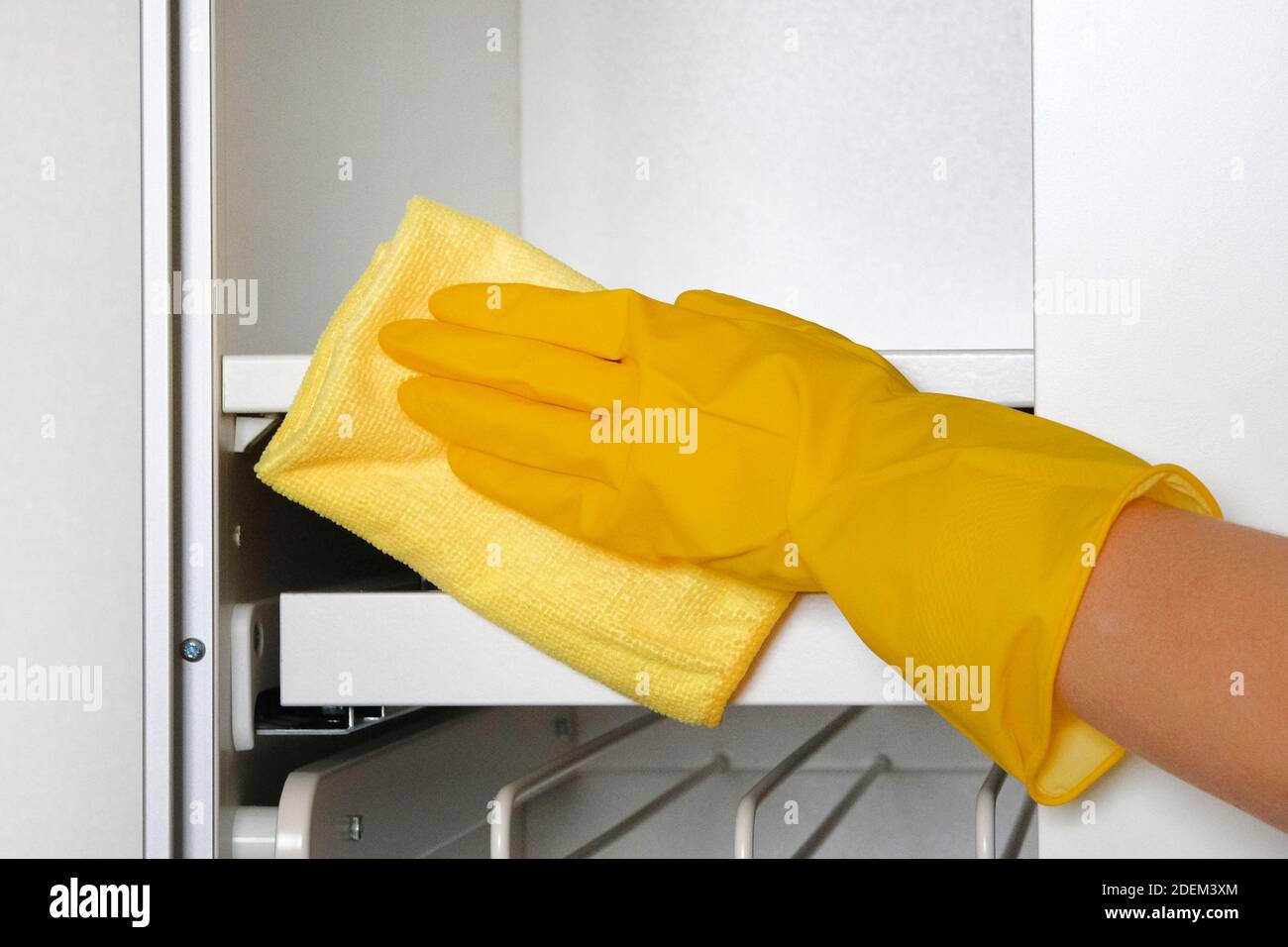 Casalinga che indossa guanti protettivi sta facendo lavoro domestico. Il guanto protettivo giallo a mano strofina i mobili bianchi con lo straccio. Foto Stock