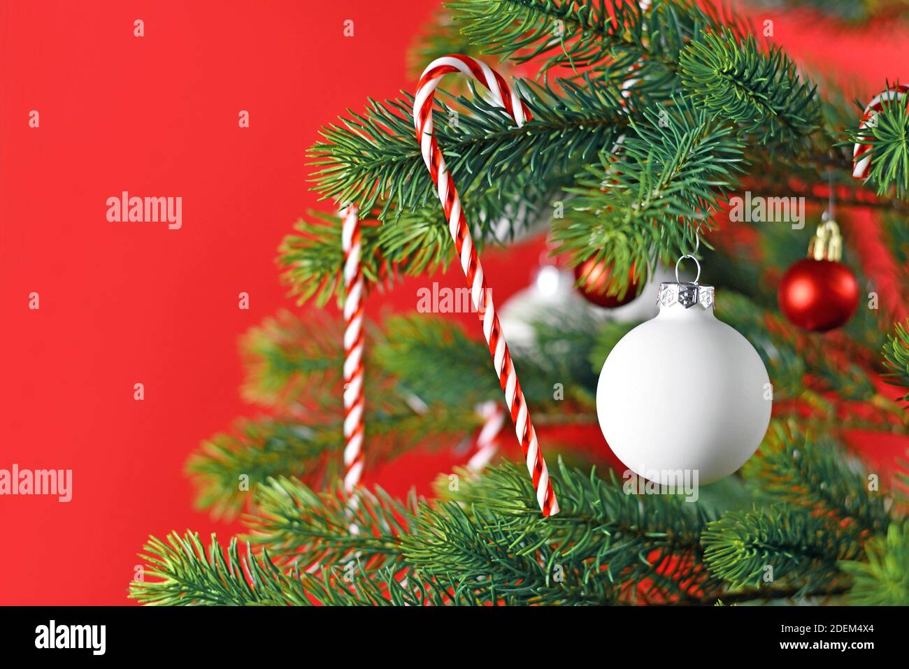 Close up di albero di Natale decorato con il bianco e il rosso albero stagionali ornamenti come e baubles candy canes su sfondo rosso Foto Stock