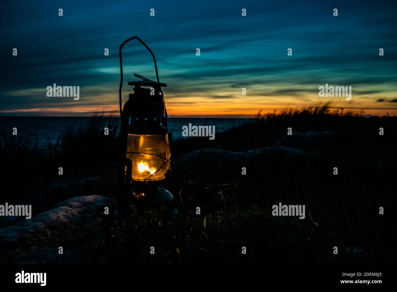 Vecchia classica lanterna a olio che brucia con una fiamma arancione vicino all'oceano al tramonto. . Foto di alta qualità Foto Stock