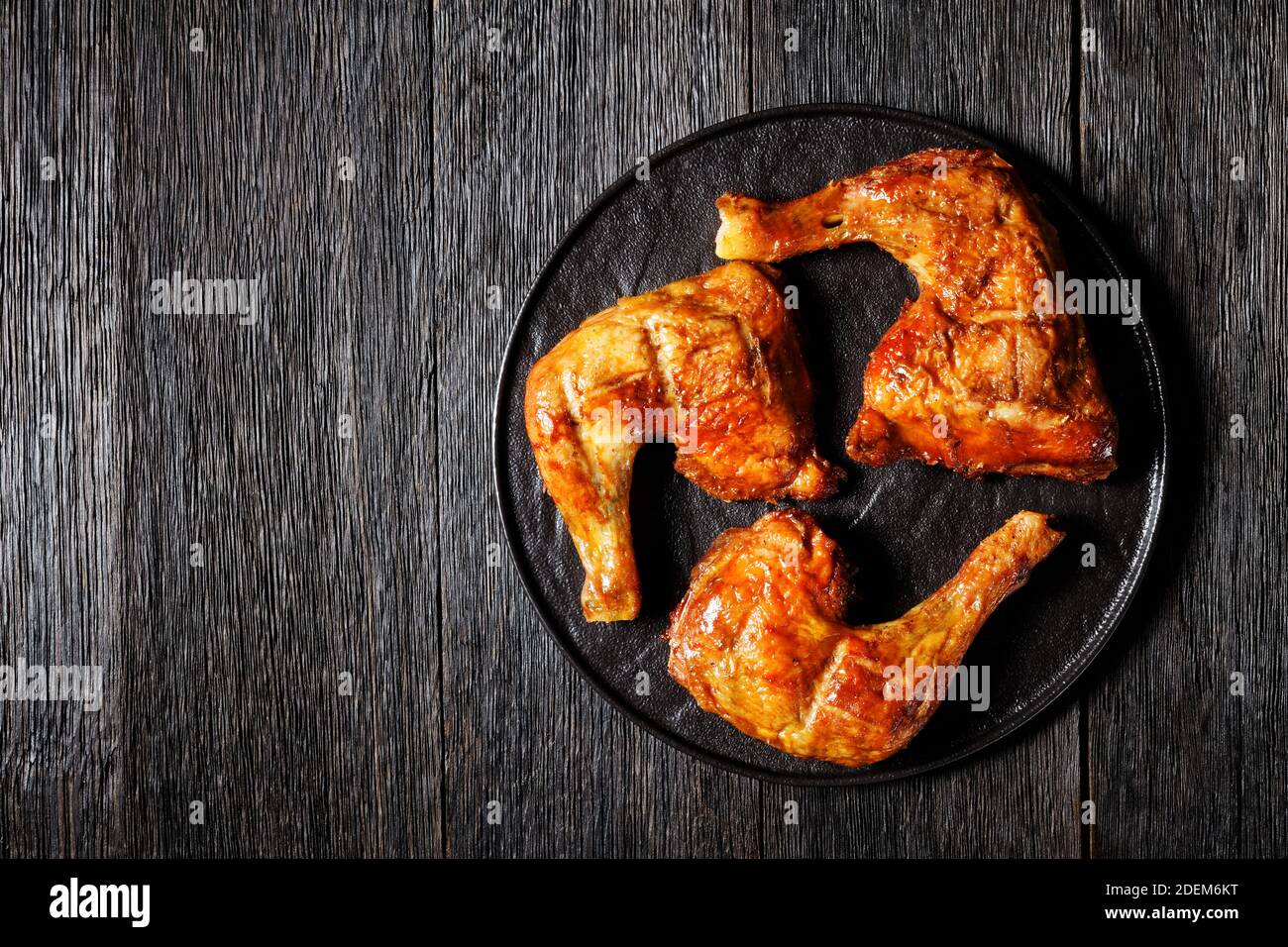 Quarti di coscia di pollo, cotti al forno, pelle-sopra, osso-in, serviti su un piatto nero, vista dall'alto, primo piano Foto Stock