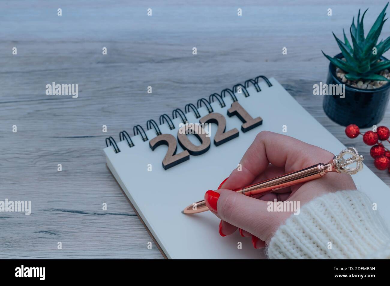 Obiettivi e concetto di risoluzione di nuovi anni. Mano femminile che tiene una penna, taccuino vuoto, numeri di legno 2021 e decorazioni natalizie isolato su un legno Foto Stock