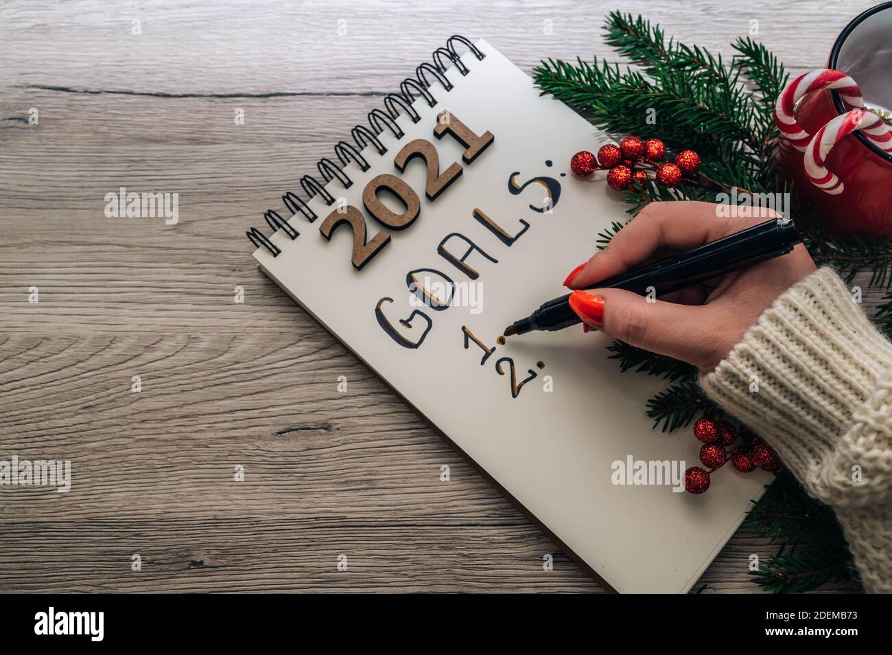 Concetto di obiettivi. Elenco degli obiettivi del nuovo anno 2021. Mano femminile che tiene una penna, taccuino e decorazioni natalizie isolato su uno sfondo di legno con copia spac Foto Stock