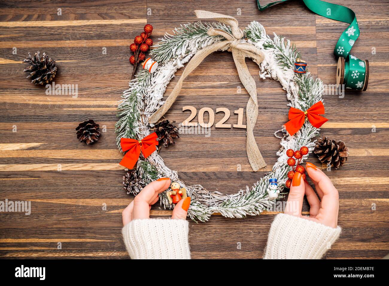 Cornice di corona da legno di pino e decorazioni natalizie e mani femminili su sfondo di legno. Disposizione piatta, stile elegante. Natale, Capodanno, preparazione per il Foto Stock
