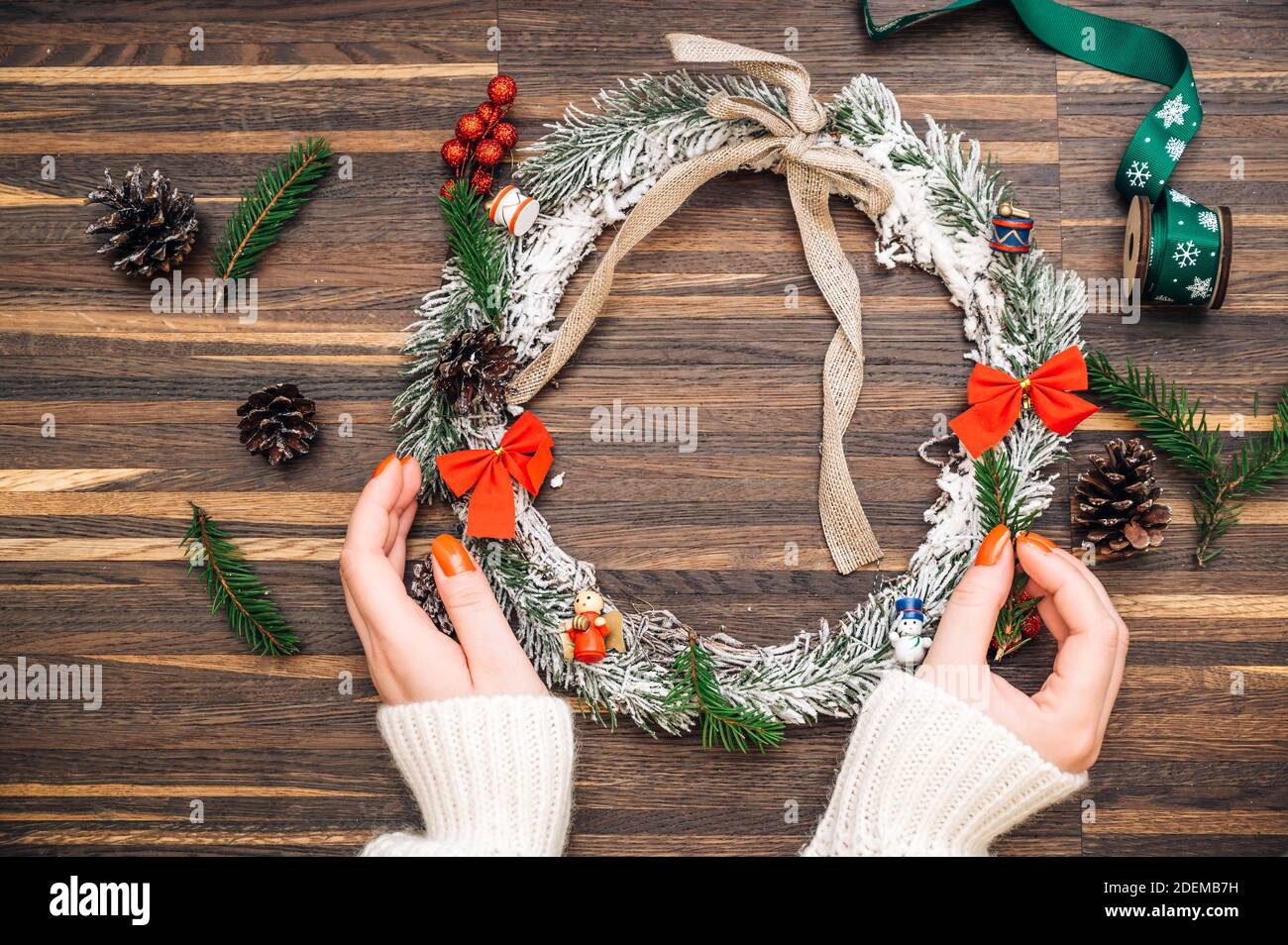 Cornice di corona da legno di pino e decorazioni natalizie e mani femminili su sfondo di legno. Disposizione piatta, stile elegante. Natale, Capodanno, preparazione per il Foto Stock