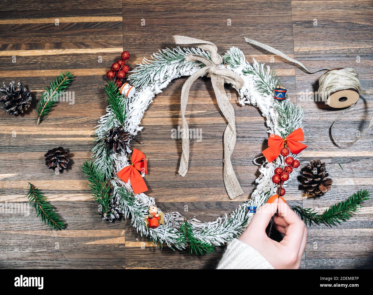 Cornice di corona da legno di pino e decorazioni natalizie e mani femminili su sfondo di legno. Disposizione piatta, stile elegante. Natale, Capodanno, preparazione per il Foto Stock