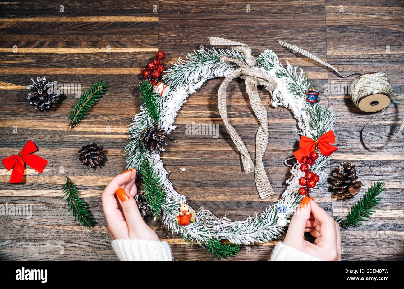 Cornice di corona da legno di pino e decorazioni natalizie e mani femminili su sfondo di legno. Disposizione piatta, stile elegante. Natale, Capodanno, preparazione per il Foto Stock