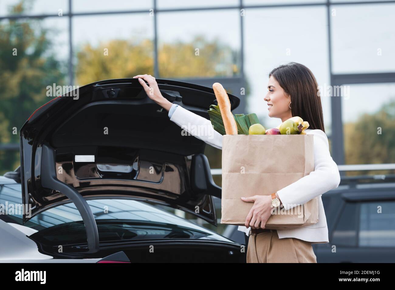 donna sorridente che apre il bagagliaio dell'auto mentre tiene la borsa per  la spesa con cibo Foto stock - Alamy