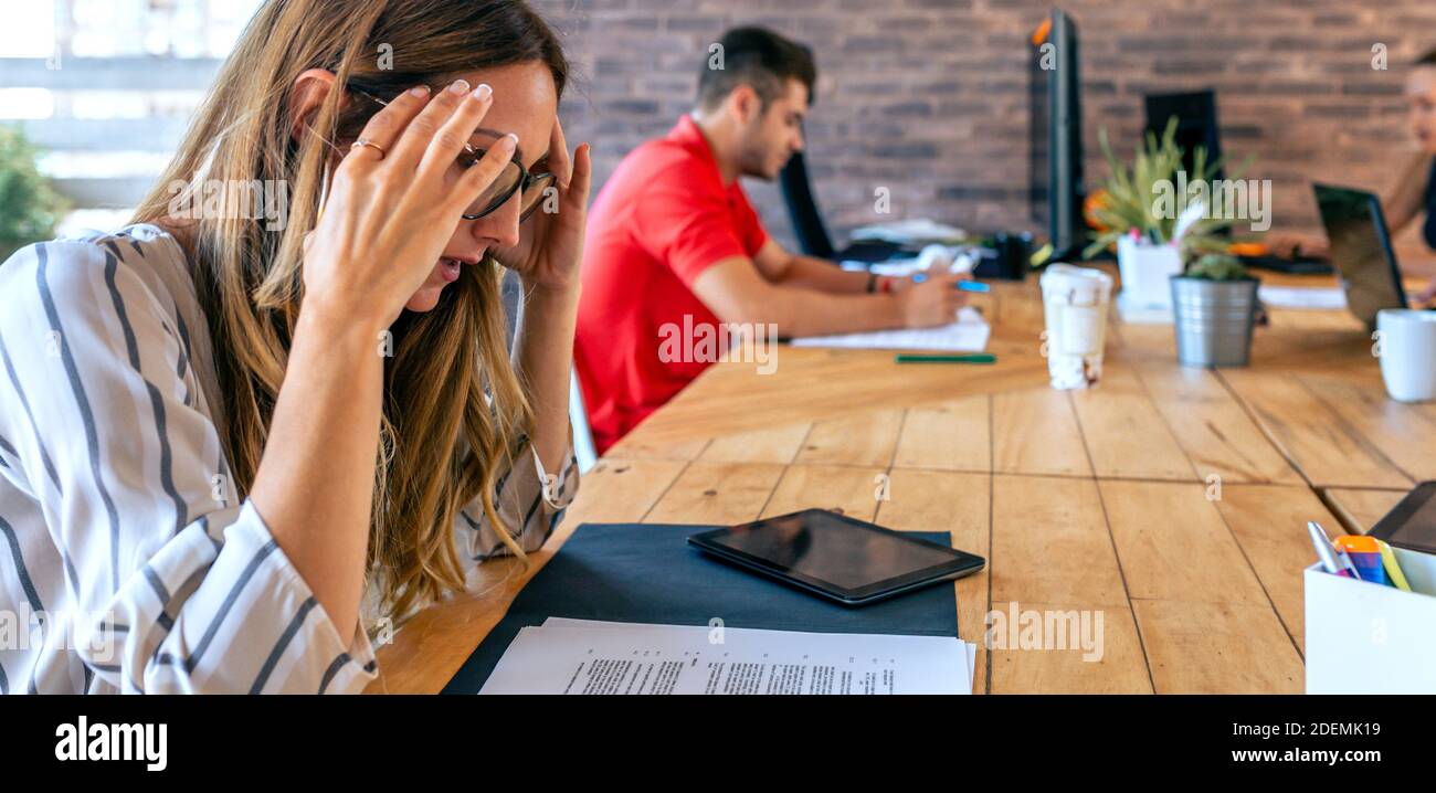 Donna d'affari stressata con le mani sulla testa che guarda i documenti Foto Stock