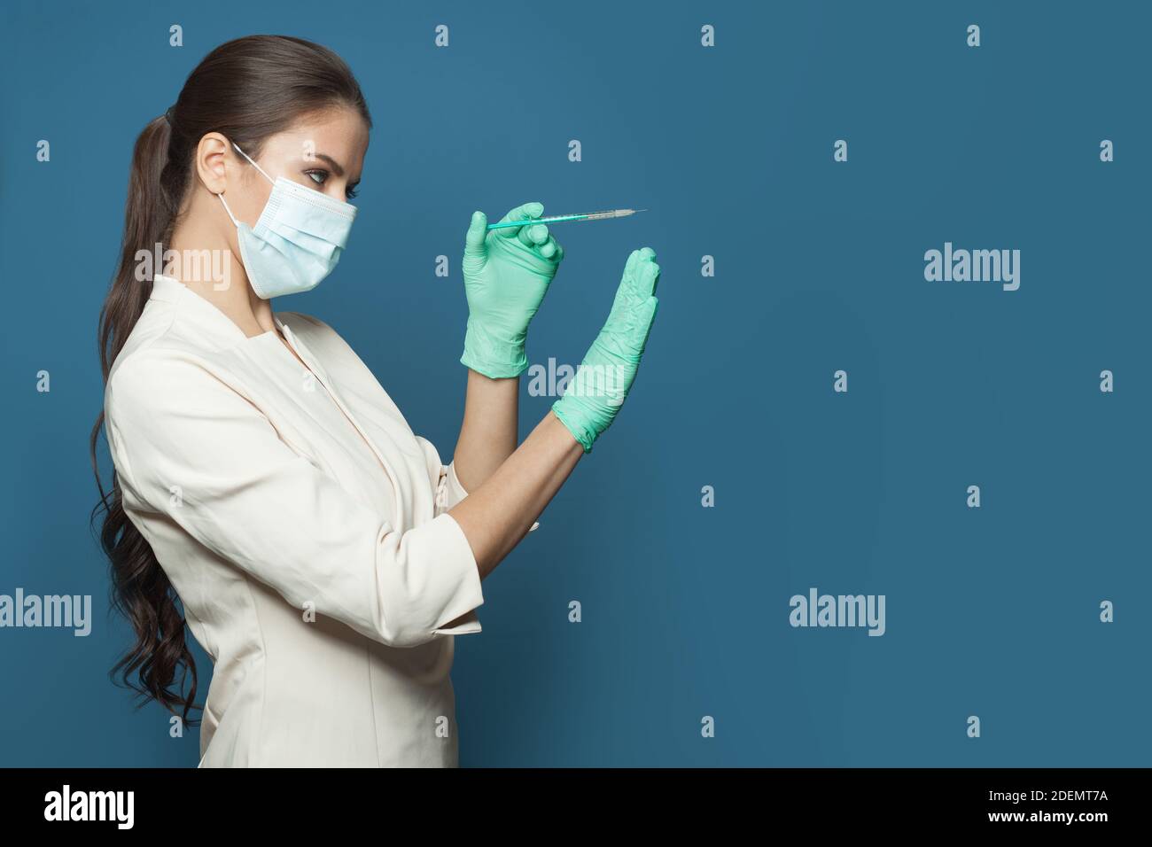 Infermiere o dottoressa che indossa uniforme medica professionale e maschera facciale protettiva che tiene la siringa su sfondo blu. Medicina, sicurezza e vaccinatio Foto Stock