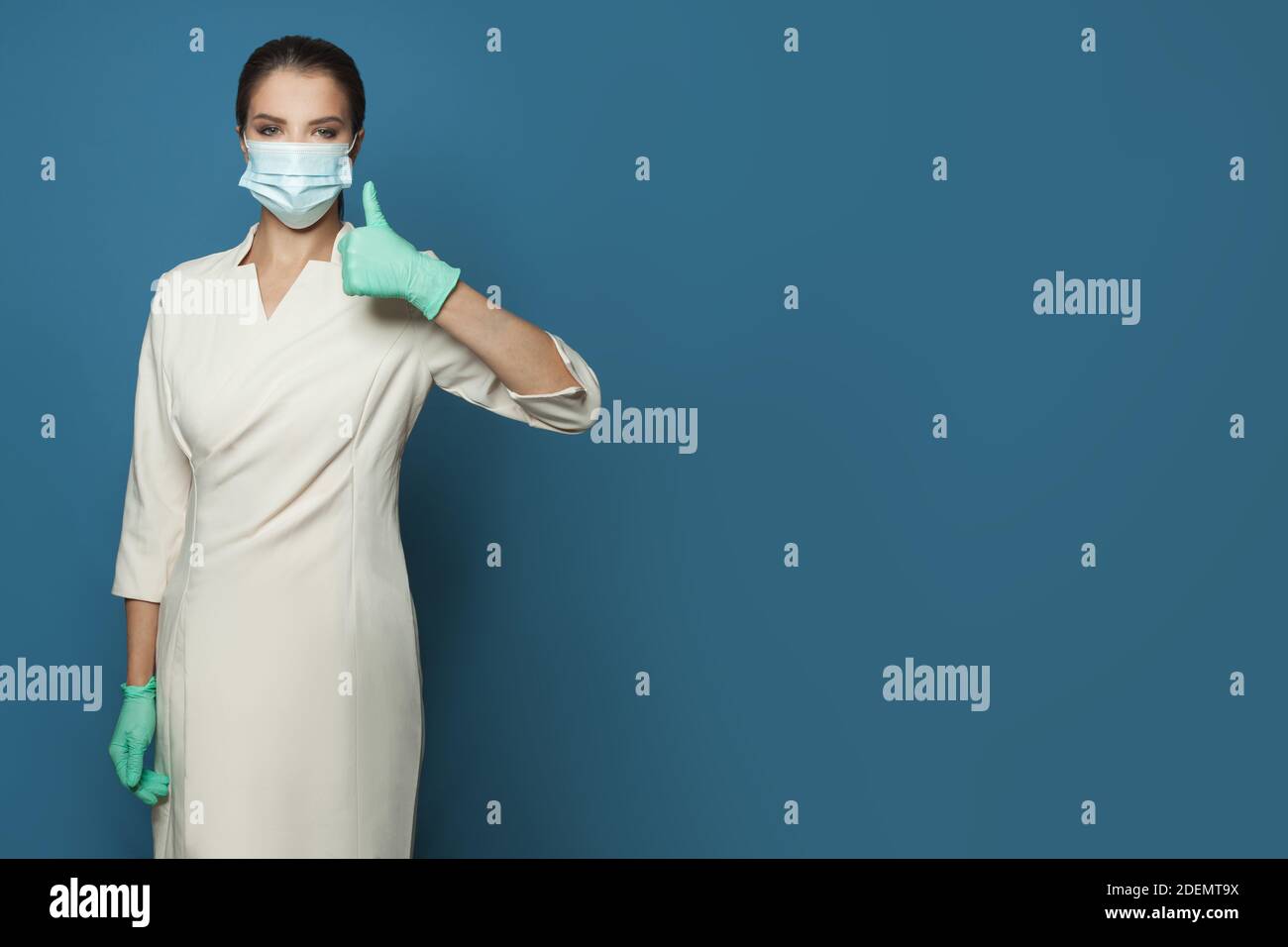 Donna medico in uniforme professionale e maschera protettiva che mostra il pollice su sfondo blu banner. Medicina, sicurezza, vaccinazione e virus covid-19 Foto Stock