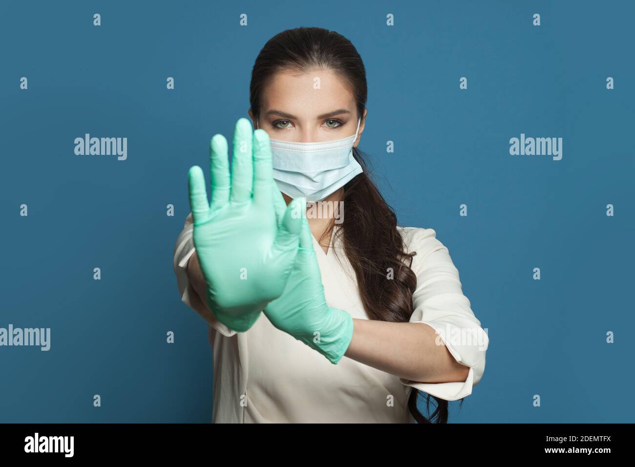 Donna medico in maschera medica protettiva che mostra il gesto di arresto su sfondo blu. Medicina, sicurezza, vaccinazione e protezione del virus covid-19 concetto Foto Stock