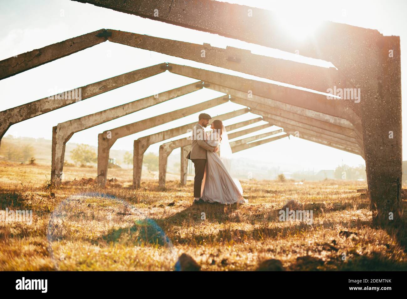 Giovane sposa e sposo coppia su un campo con vecchi archi alla luce del sole. Foto Stock