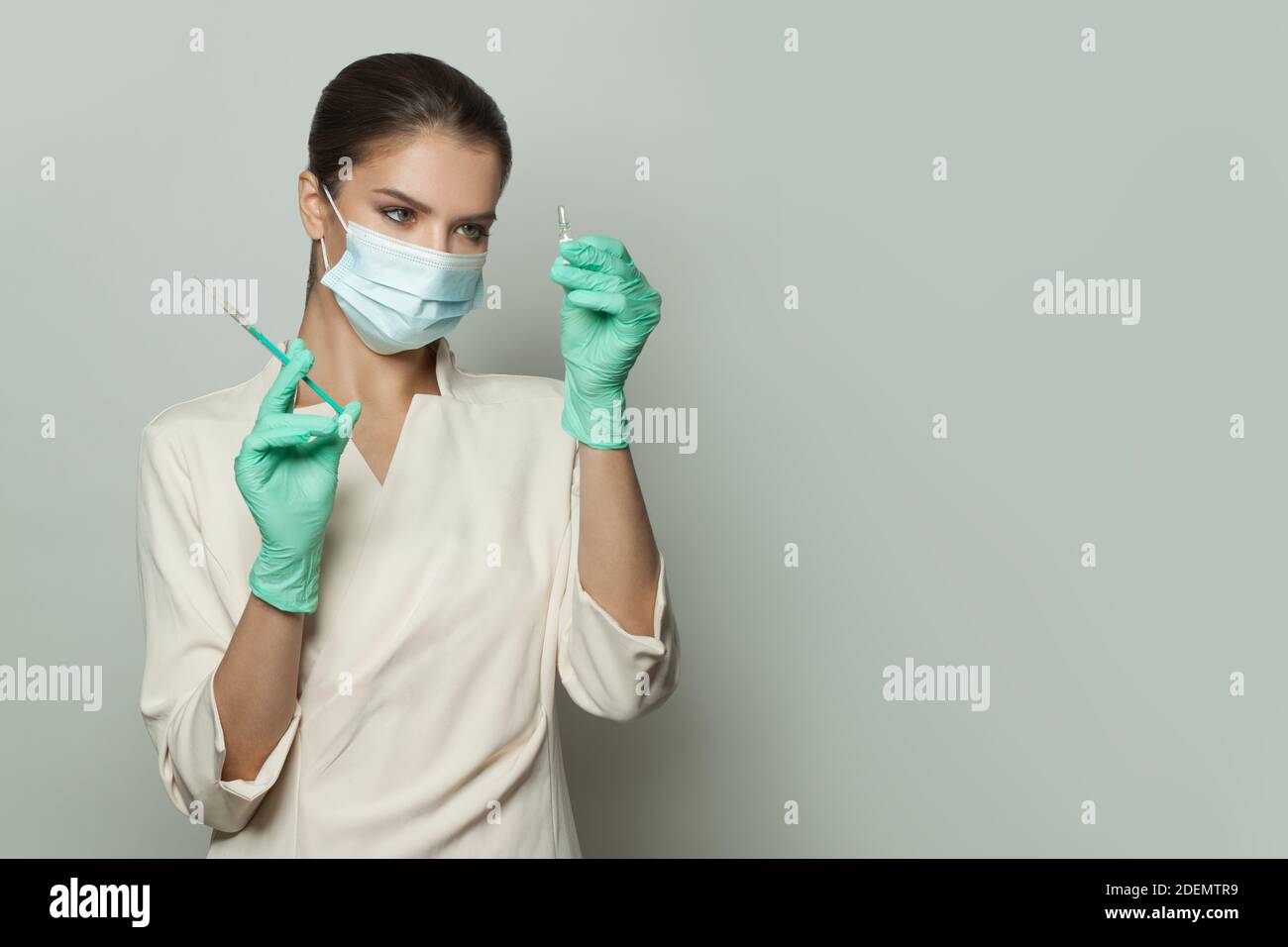 Medico in uniforme professionale e maschera medica che contiene siringa e ampolla iniezione su sfondo bianco. Medicina, cosmetologia e vaccinazione conce Foto Stock