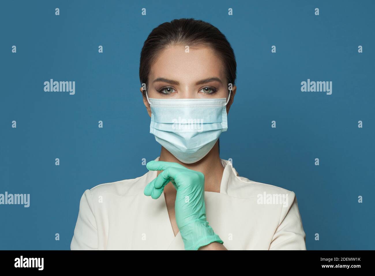 Ritratto di medico che indossa maschera medica protettiva e uniforme professionale su sfondo blu. Medicina, cosmetologia e concetto di vaccinazione Foto Stock