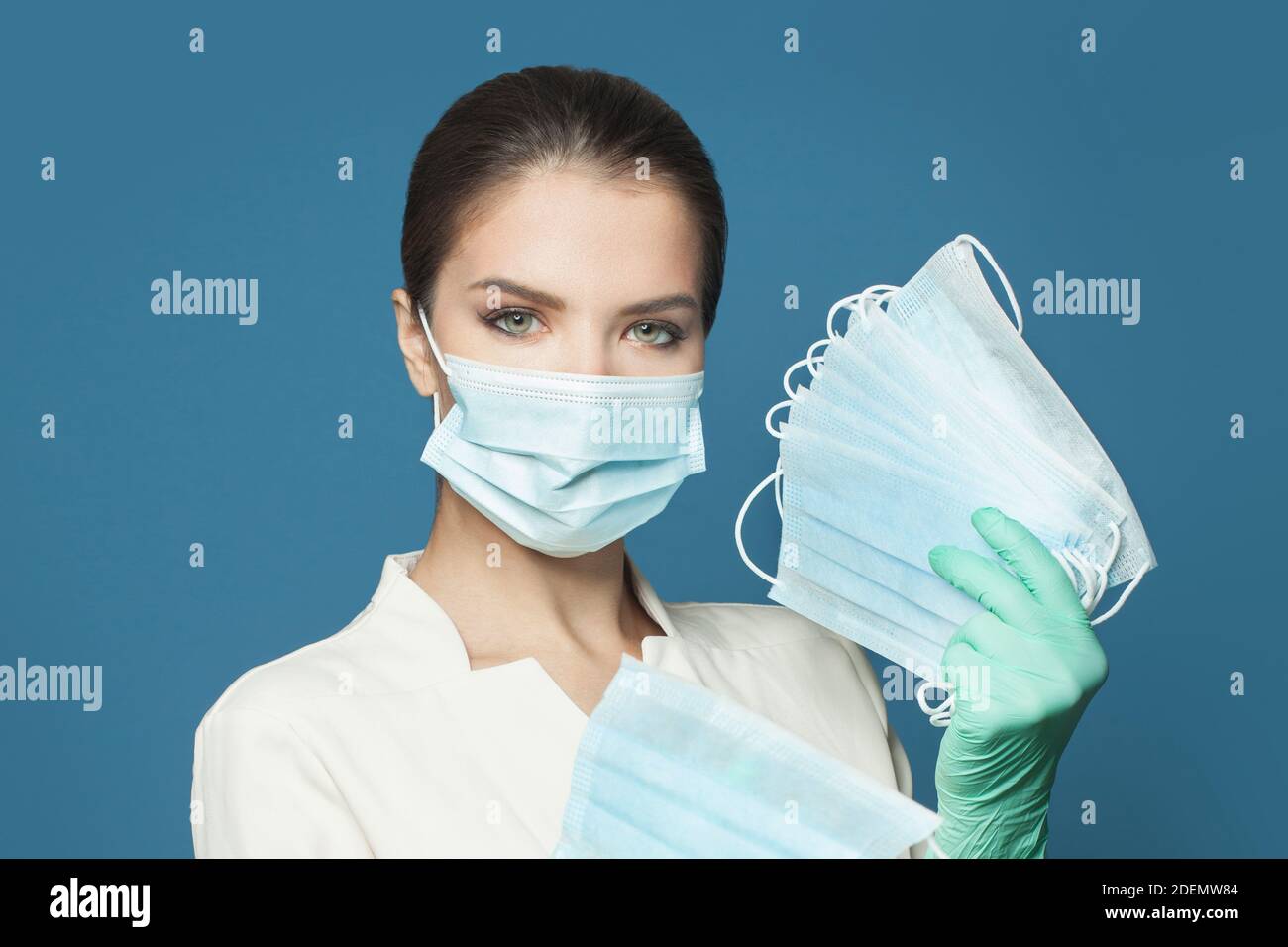 Medico che tiene molte maschere mediche protettive su sfondo blu. Medicina e concetto di sicurezza Foto Stock