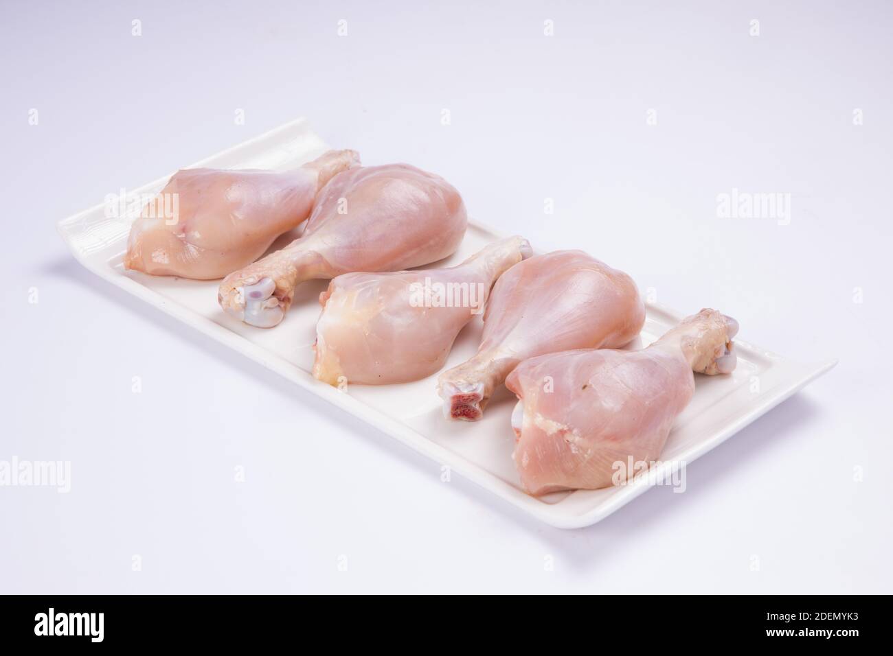 Bastoncini di pollo crudi disposti su stoviglie da tavolo bianche sfondo di colore bianco Foto Stock