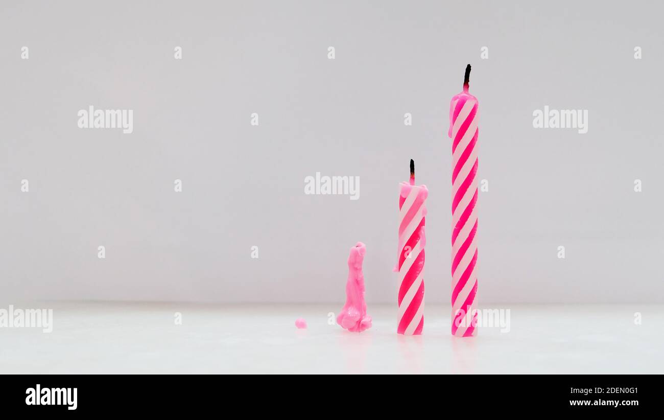 Tre candele di compleanno rosa estintate in diverse altezze, poste in cima ad una superficie fianco a fianco da corto a alto. Foto Stock